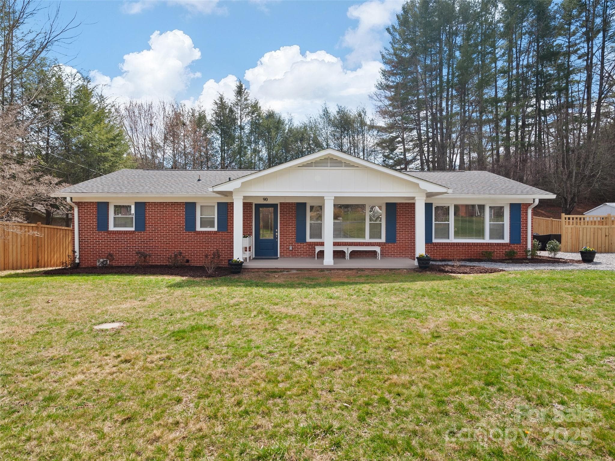 Red brick ranch house with blue shutters and a white gabled front porch.