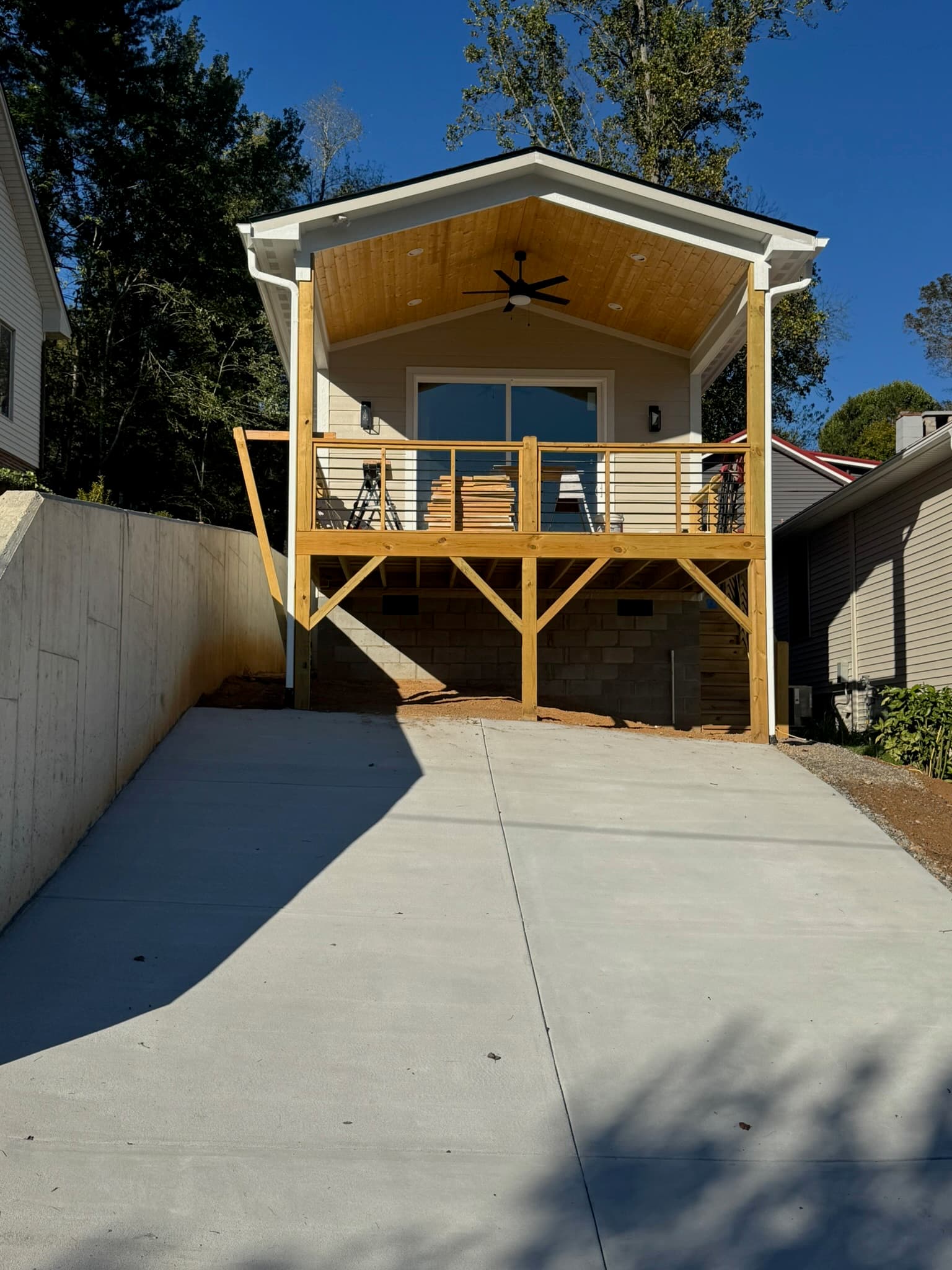 Elevated wooden deck with a covered porch and ceiling fan above a smooth concrete driveway.