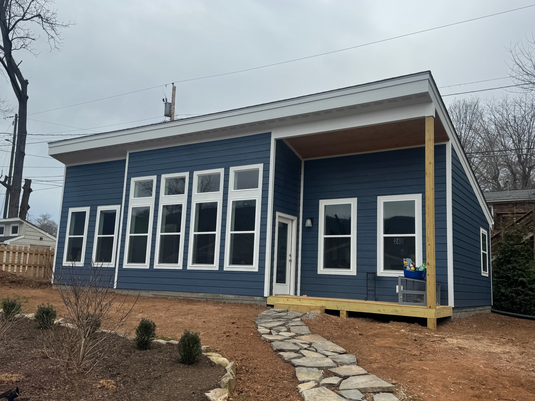 Modern blue house with white trim, large windows, and a stone path in dirt yard.